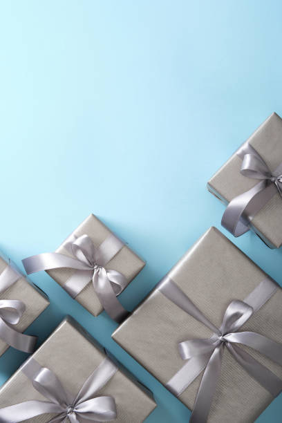 istock Gray gift boxes with silver ribbons on light blue background. Vertical, space for your text. 2112486487