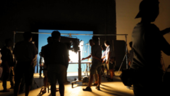 Blurry images of making video production shooting studio in silhouette which have professional equipment such as camera, tripod and blue screen backdrop set for chroma key technique in post process
