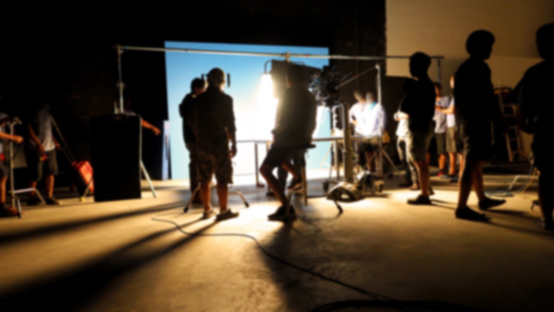 Blurry images of making video production shooting studio in silhouette which have professional equipment such as camera, tripod and blue screen backdrop set for chroma key technique in post process