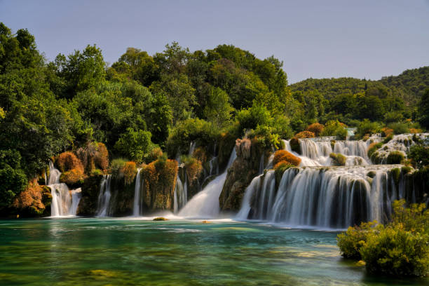 istock Waterfall cascading in lush forest with rocks and trees 2112500939