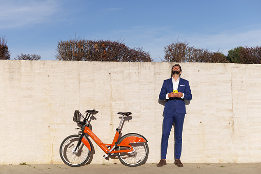 Business man looking up to the sky. Bicycle leaning on wall. Sky background copy space. High quality photo