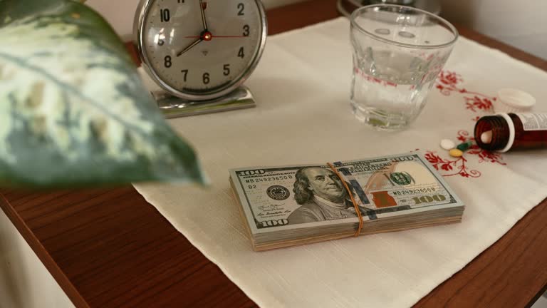 Stack of US dollar banknotes and drugs on night stand