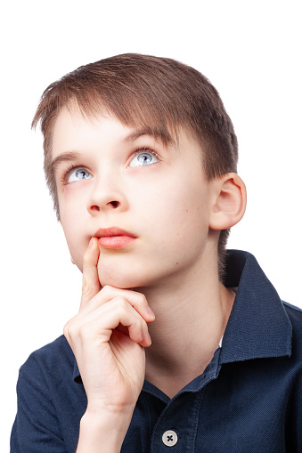 A young boy wearing blue polo shirt looking up with a thoughtful expression. Studio portrait against white background