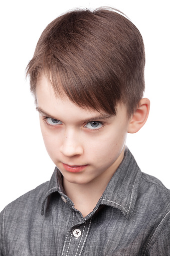 A young boy wearing denim shirt gazing intently at the camera giving a disapproving look. Studio portrait against white background