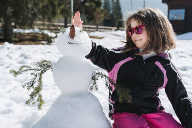 Beautiful young woman building a snowman outdoors in the wintertime.