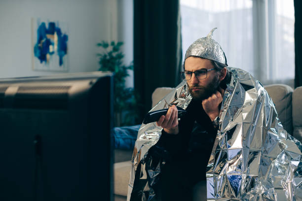 A man in a tinfoil hat watches TV. A man in a tinfoil hat watches TV. tinfoil barb barbonymus schwanenfeldii stock pictures, royalty-free photos & images