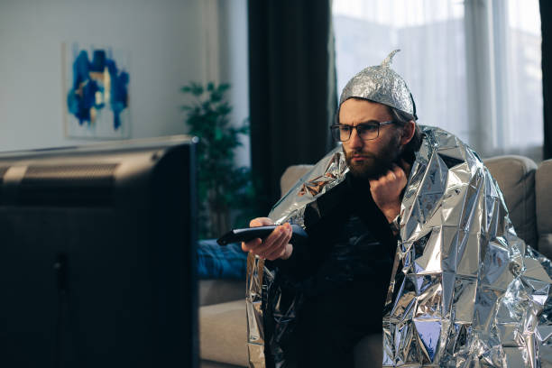 A man in a tinfoil hat watches TV. A man in a tinfoil hat watches TV. tinfoil barb barbonymus schwanenfeldii stock pictures, royalty-free photos & images