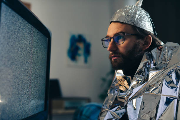 Man in Tin Foil Hat and Blanket Watching TV Interference Man in Tin Foil Hat and Blanket Watching TV Interference tinfoil barb barbonymus schwanenfeldii stock pictures, royalty-free photos & images