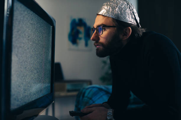 Man in Tin Foil Hat and Blanket Watching TV Interference Man in Tin Foil Hat and Blanket Watching TV Interference tinfoil barb barbonymus schwanenfeldii stock pictures, royalty-free photos & images