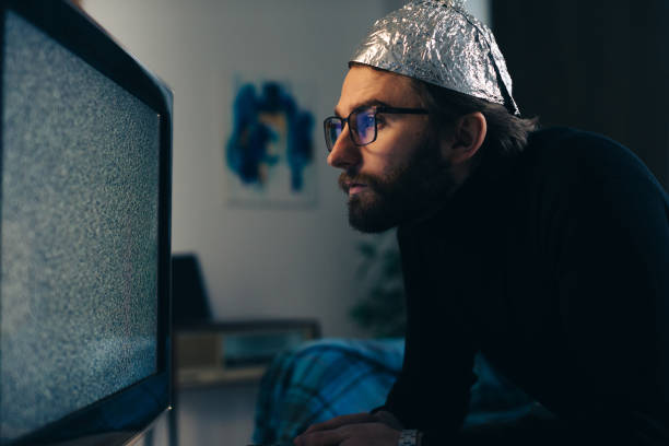 istock Conspiracy Theory on Screen: Man in Tin Foil Hat and Blanket Observing TV Interference 2112599909