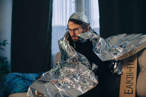 istock A man in a tinfoil hat is wrapped in a tinfoil blanket on the sofa at home. 2112601000
