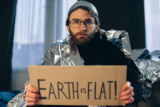 Flat Earth Advocate: Man in Tin Foil Hat and Blanket Holds Sign 'Earth is Flat