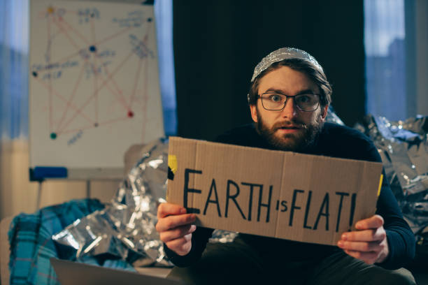 Championing Pseudoscience: Man Holding 'The Earth is Flat' Sign Championing Pseudoscience: Man Holding 'The Earth is Flat' Sign tinfoil barb barbonymus schwanenfeldii stock pictures, royalty-free photos & images
