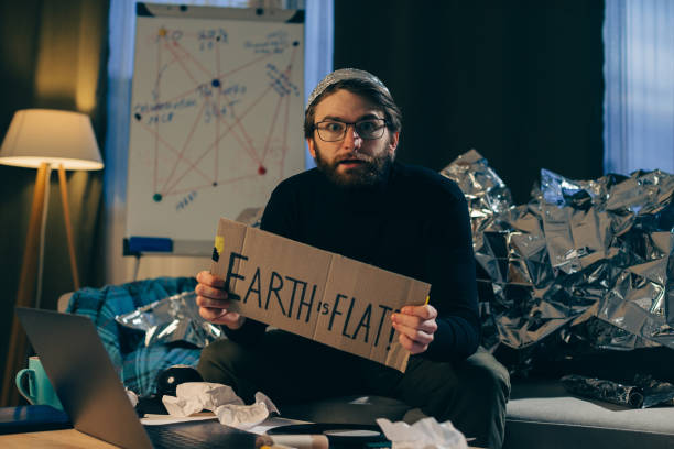 Supporting Pseudoscience: Man Holds Sign Asserting 'The Earth is Flat Supporting Pseudoscience: Man Holds Sign Asserting 'The Earth is Flat tinfoil barb barbonymus schwanenfeldii stock pictures, royalty-free photos & images