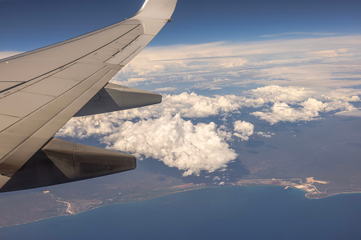 A beautiful view of the blue sky with fluffy white clouds during a flight over the coastline of the Atlantic Ocean, as seen from the airplane window.