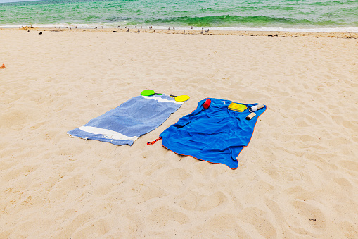 Close-up view of two beach towels and various household items laid out on the sandy shores of the Atlantic Ocean beach. Miami Beach.