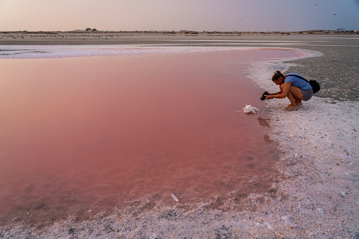 One woman crouches down to photograph the crystalize salt at Pink lake of Jalan Bani Bu Ali at sunset. Oman