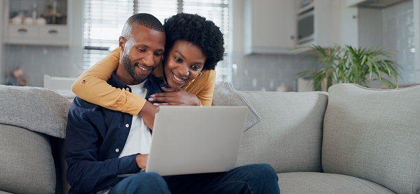 Loving happy couple sitting on couch at home, embracing, using laptop computer, young man and woman watching movie online, copy space.