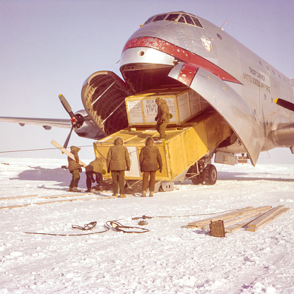 Alaska, USA - between 1955 and 1957: Five men in parkas unloading a US Air Force C-124A cargo plane through the front clamshell doors on a snow covered landing strip. The 4th Military Airlift Squadron transported radar equipmnt to Alaska for the Distant Early Warning Line, part of th US Cold War defense.