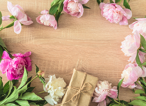 frame of pink peonies flowers and craf gift box on a wooden background; copy space