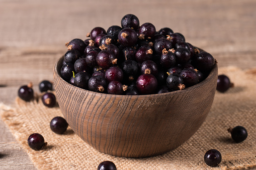 Black currant in a bowl on wooden background. Organic berries.