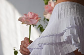 A bride girl in a white dress holds a delicate pink rose flower in her hand.