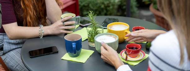 Horizontal banner or template with close-up of the table set for breakfast with cappuccino and coffee - Mobile phones on the table -  Friends having fun together at hostel dehors