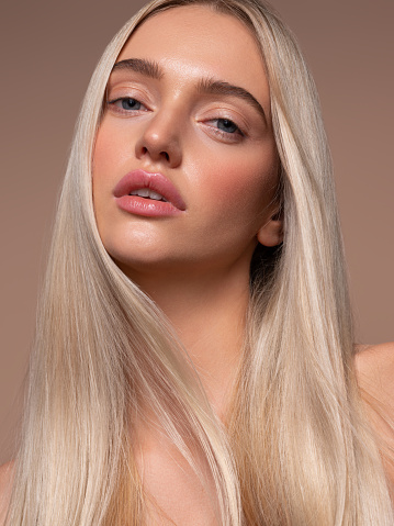 Portrait of nicely looking young model with dyed in the blond shade hair and dressed in a bright evening make-up.Perfect model straightly gazing by kind, tender look at the viewer. Hairstyling,dye of hair, cosmetics and make-up.