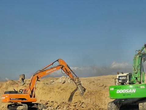 Cairo, Egypt, March 23 2024: demolition hydraulic crawler excavators and vehicles removing prats from a desert roadside to develop and widen the highway, Egyptian real estate road development, selective focus
