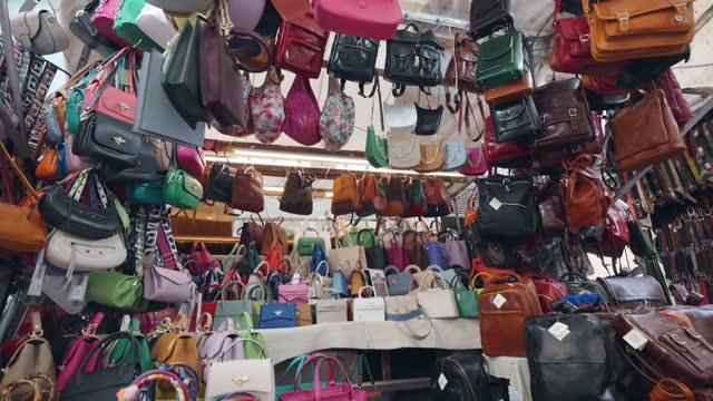 Florence market stall with variety of genuine leather products, colourful bags, backpacks, wallet and other accessories on bazaar counter, tourist shopping in Florence