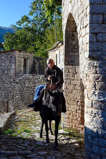 Kalarrytes, Greece - October 25, 2019: A man rides his mule in a traditional village of Epirus