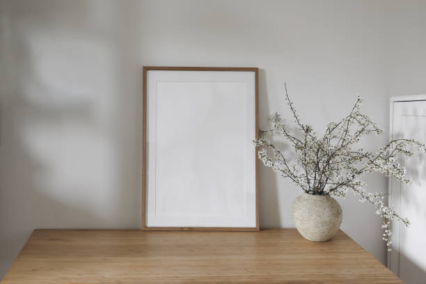 istock Vertical wooden picture frame, poster mockup in sunlight. Spring composition. Elegant interior, home office still life. Artistic display. Blooming cherry plum tree branches in vase. Wooden table, desk 2112850361