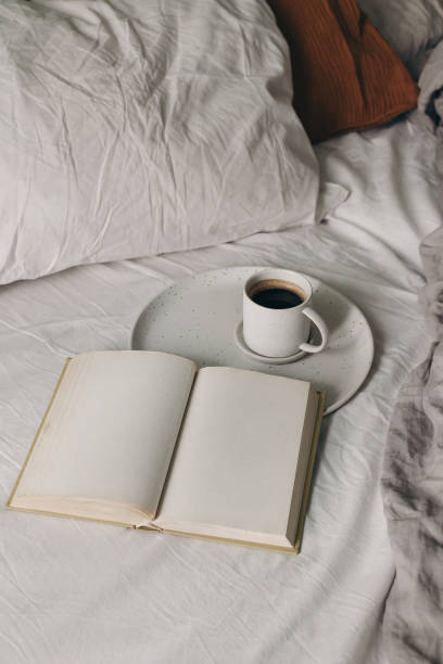 istock Cup of coffee, espresso. Open book, diary mockup on white bed sheet. Breakfast in bed concept. Blurred muslin, linen pillows, blanket. Scandinavian bedroom. Vertical top view. Lifestyle banner. 2112851395