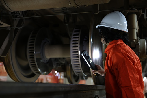 Male engineer checking the train parts from below the undercarriage at the railway maintenance workshop