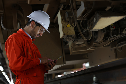 Male engineer checking the train parts from below the undercarriage at the railway maintenance workshop