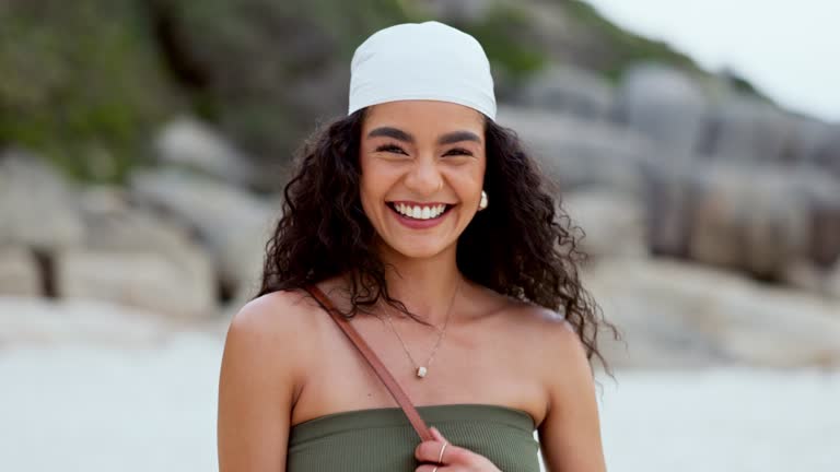 Woman, face and walking on beach, smiling and comedy in outdoors or travel to ocean for fun. Happy female person, portrait and laughing for humor in nature, freedom and relaxing on holiday or getaway