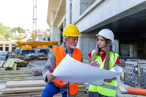 Young Woman and her Senior Manager are Looking at Paper Plans at Construction Yard.