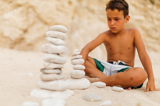 Boy sitting on the beach and  balancing stack of stones