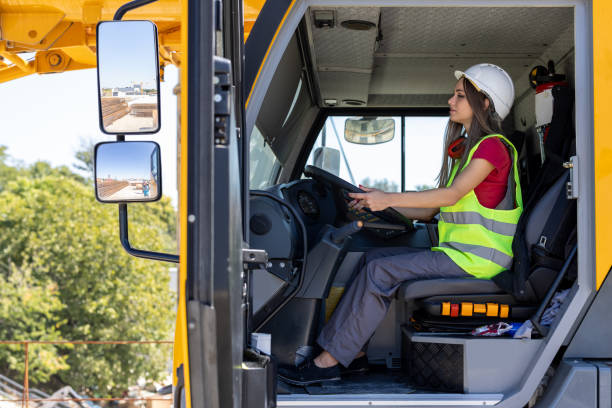 A mature Caucasian man with a close-cropped beard sits confidently inside a pushback tug, dressed in a hi-vis vest and grey work attire, ready for towing operations at an airport ramp.