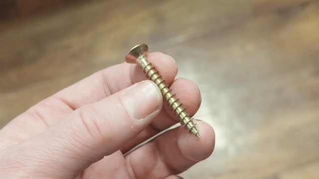 Man's hand holds metal self-tapping screw, close-up.