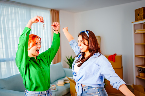 Homeowners. Happy young caucasian couple young women holding  house flat apartment keys, celebrating new purchase buying real estate