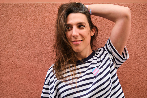 Lesbian trans woman smiling with long hair wearing transgender flag pin.