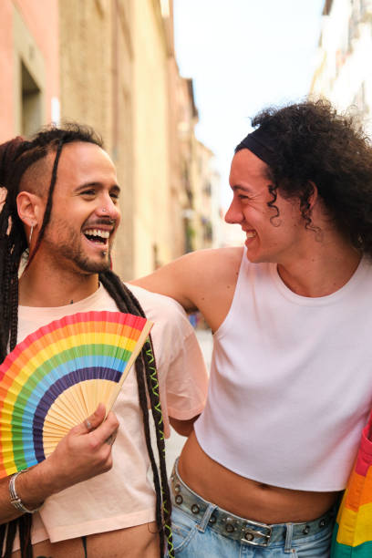istock Gay couple laughing and smiling while walking down a street during Pride Parade. 2112971808
