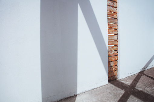 A white concrete wall made with obvious creativity. The vertical gap is filled with wooden slats, which makes the structure beautiful and stylish. Light and shade background.