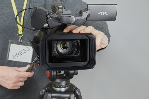 Video operatorâs hands bring the camera into focus, close-up of the cameraman at work, a video camera with a wide-angle lens in a manâs hands.