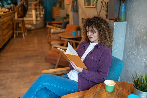 Woman sitting at coffee shop drinking coffee and reading a book