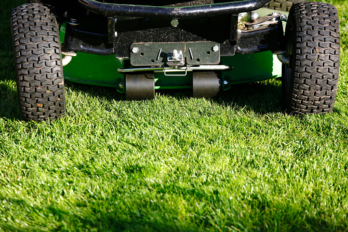 Motorized riding lawn mower close-up at a sunny summer day on a green grass.