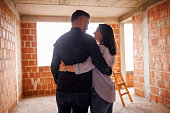 Rearview shot of a young embraced couple at their new house under construction, planning future and dreaming