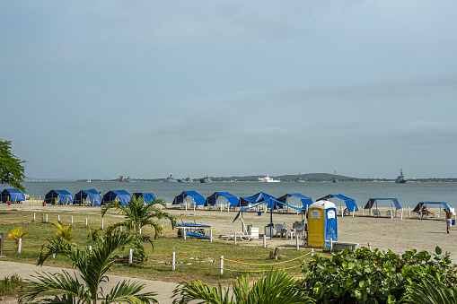 Cartagena, Colombia - July 25, 2023: Bocagrande. Looking south over Playa Castillo Grande beach with blue tents over the bay to Isla Tierra Bomba island. Ships on the water, light blue sky