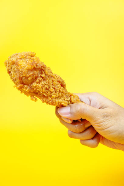 istock Female hand holding fried chicken on yellow background. 2113151779